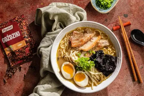 Jak zrobić ramen? Aromatyczny bulion, makaron, jajko na pół, chrupiąca wieprzowina i nori. Obok paczka goździków Prymat.