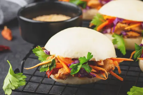 Saftiger bao burger mit Hähnchen, Karotten, Rotkohl und Koriander auf einem Rost.