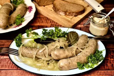 Saure Bratwurst mit Zwiebeln und Petersilie auf einem Teller, dazu Brot und ein Glas Senf.