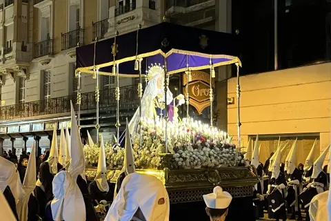 Procesión del Santo Entierro en Zaragoza. Figuras religiosas iluminadas por velas, rodeadas de nazarenos con túnicas y capirotes blancos.