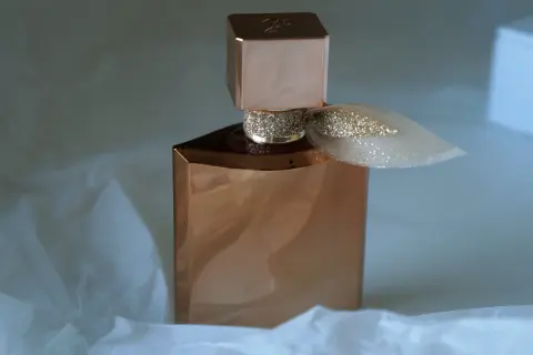 Elegancka butelka perfum Lancome Eclat w kolorze miedzi, ozdobiona brokatową wstążką, otulona delikatnym białym papierem.
