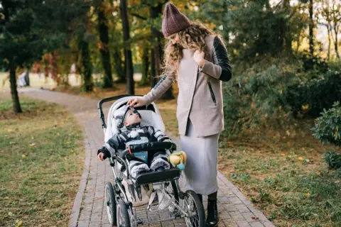 Mama poprawia czapkę malucha, który siedzi w spacerówce. Jesienny spacer po parku.