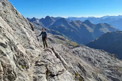 Wanderer auf dem Heilbronner Weg, gesichert an einem Stahlseil, genießt die atemberaubende Bergkulisse.