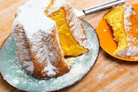 Une brioche italienne pandoro, saupoudrée de sucre glace, est servie sur une assiette bleue. Une part est sur une assiette orange.