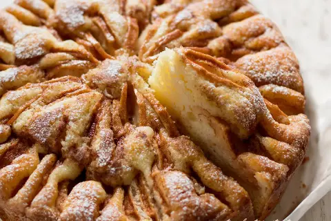 Una deliziosa torta di mele, cosparsa di zucchero a velo, con una fetta sollevata che rivela la morbida consistenza.