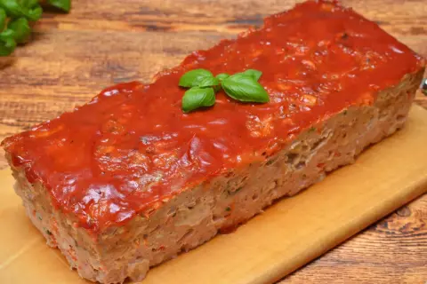 Pyszny, domowy meatloaf z sosem pomidorowym i listkami bazylii, gotowy do podania na desce.