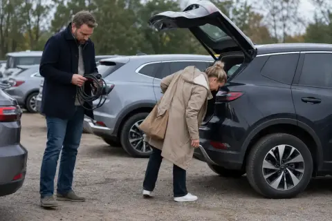 Man med laddkabel vid en begagnad elbil. Kvinna tittar i bagageluckan på en annan elbil.