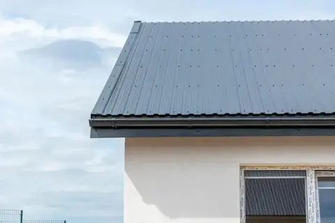 Nowy dach z szarej blachy trapezowej, zamontowany na domu. Montaż blachy trapezowej zakończony sukcesem, budynek gotowy na każdą pogodę.