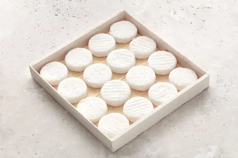 Un plateau en bois présente une rangée de petits fromages ronds, évoquant l'origine du saint marcellin fromage.