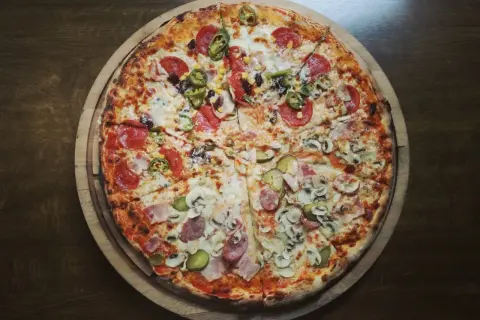 Pizza podzielona na cztery części z różnymi dodatkami: salami, jalapeno, kukurydza, pieczarki, ogórek, szynka.