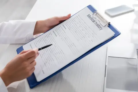 Manos de médico revisan un historial médico en un portapapeles, preparándose para un certificado médico A2.