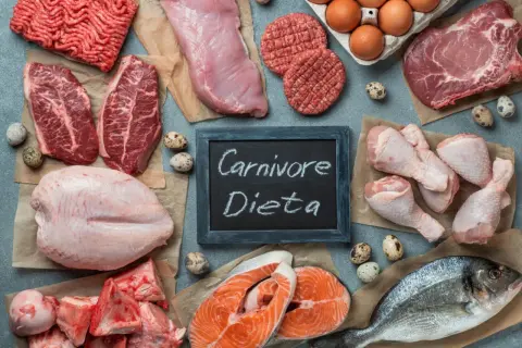 Różnorodne mięsa i ryby, jajka, kości. Tabliczka z napisem "Carnivore Dieta" sugeruje, że to składniki diety mięsożercy.