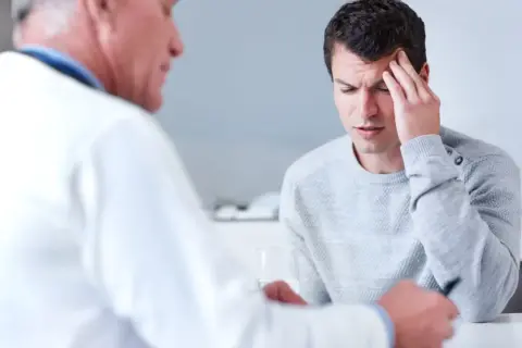 Ein Mann mit Kopfschmerzen spricht mit einem Arzt. Die Diagnose: ein gutartiger hirntumor.