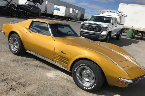 Złoty Chevrolet Corvette Stingray, klasyk wśród amerykańskich samochodów, stoi obok białej ciężarówki.