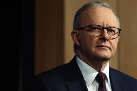 Primo piano di Anthony Albanese, uno dei più noti personaggi famosi australiani, con occhiali e abito scuro.