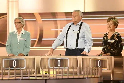Trzech uczestników programu "Koło Fortuny" - Marianna, Władysław i Anna - stoi przy swoich stanowiskach.