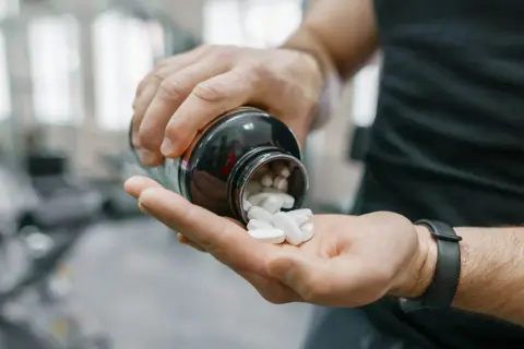 Uomo in palestra versa creatina in polvere nella mano. Ottimizza i tuoi allenamenti: scopri creatina quando assumerla per massimizzare i risultati.