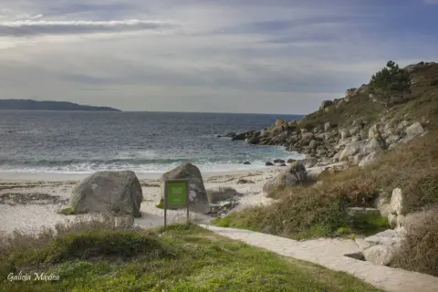 La playa de ancoradouro, con su arena blanca, rocas imponentes y el mar azul, invita a la contemplación. Un sendero de piedra serpentea hacia la costa.