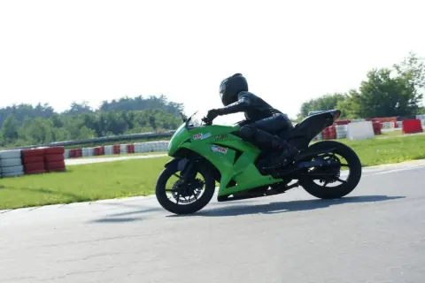 Motocyklista w kombinezonie na zielonym motocyklu ściga się na torze wyścigowym.