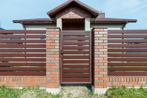 Eleganckie ogrodzenie z klinkieru i brązowych paneli, z solidną bramą wjazdową, stanowi ozdobę posesji.