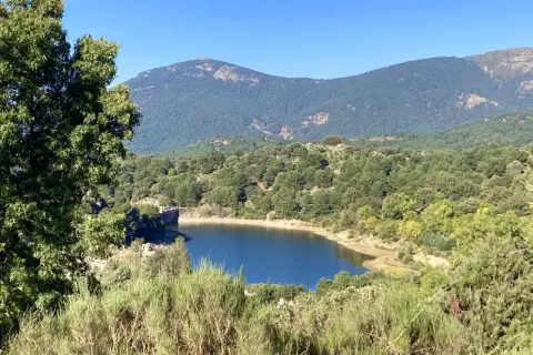El embalse de Navalmedio, rodeado de bosques y montañas, refleja el cielo azul.