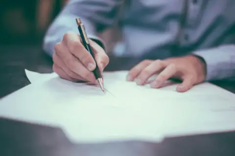 Dłoń pisze na papierze, być może notując, jak sprawdzić numer księgi wieczystej.