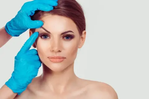 Kobieta z nieudaną plastyką powiek górnych, której oczy są badane przez lekarza w niebieskich rękawiczkach.