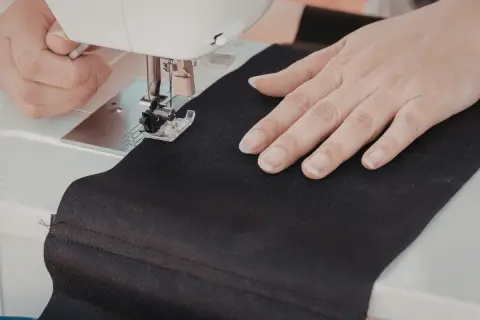 Ręce szyjące czarną tkaninę na maszynie, tworząc własną torbę DIY.