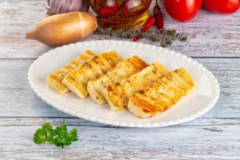 Grillowany ser halloumi na talerzu, idealny do prostych przepisów. W tle czosnek, cebula i pomidory.