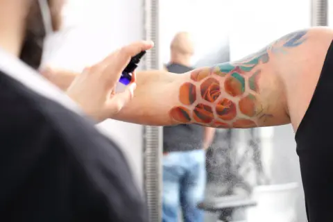 Ein frisches Tattoo mit Rosen in Wabenform wird besprüht. Der Träger ruht sich aus, während die Pflege beginnt.
