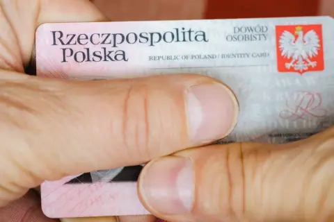 Dłonie trzymają polski dowód osobisty. Widoczna jest nazwa "Rzeczpospolita Polska" oraz godło. Widać fragmenty tekstu, w tym "seria i numer dowodu".