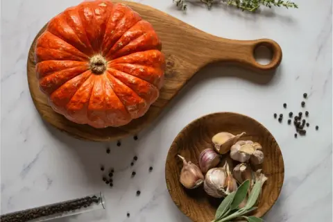 Pomarańczowa dynia muscat na drewnianej desce, obok czosnek, pieprz i zioła. Idealne składniki na jesienną zupę.
