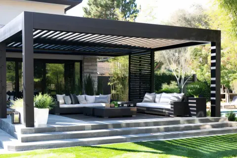 Nowoczesna, czarna pergola przed wejściem do domu, z wygodnymi sofami i stolikami, tworzy idealne miejsce do relaksu na świeżym powietrzu.