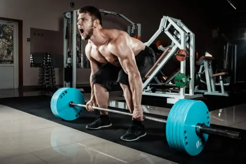 Mężczyzna z determinacją wykonuje deadlift, zaciągając sztangę z niebieskimi talerzami.