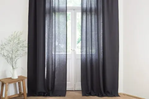 Ciemne zasłony wiszą przy drzwiach balkonowych. Wazon z gałązkami na drewnianym stołku. Jak mierzyć zasłony?