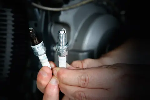 Manos sostienen bujías de moto, una nueva y otra sucia. Saber cada cuanto cambiar bujias moto es clave para el rendimiento.