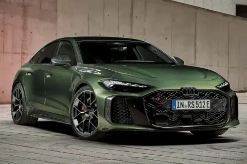 Elegancki, zielony Audi A5 Coupe z agresywnym grillem i sportowymi felgami, zaparkowany na drewnianej podłodze przy betonowej ścianie.