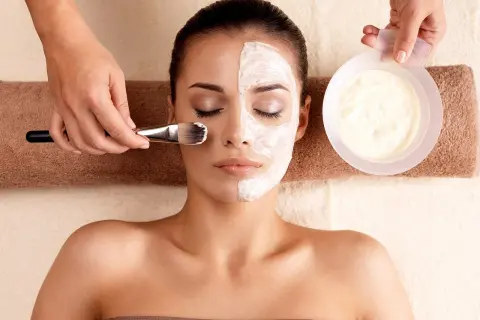 Una mujer recibe un tratamiento facial con una mascarilla aplicada con brocha.