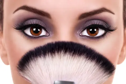 Occhi marroni intensi, evidenziati da un trucco smokey viola e ciglia lunghe, sembrano ancora più grandi e sporgenti grazie a un pennello da trucco sfocato.