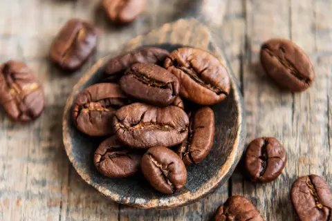 Chicchi di caffè tostati su un cucchiaio di legno, simbolo di alta qualità di caffè.