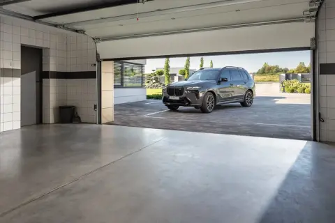 Nowoczesny garaż z betonową posadzką, idealny na jaki beton na posadzkę w garażu. Ciemny SUV czeka przed wejściem.