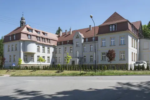 Elegancki budynek z wieżyczką, gdzie mieści się dom seniora Magda lenka, otoczony zielenią.