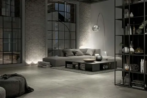 Salon industriel moderne avec canapé gris, table basse, étagères noires et **carrelage rectifié** au sol.
