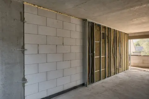 Ściana z bloczków zbrojona metalowym stelażem, w nieogrzewanym domu, czeka na karton gips. Izolacja z wełny mineralnej i instalacja elektryczna widoczne.