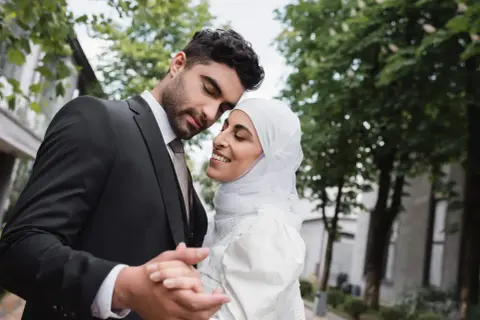 Un uomo in abito scuro e una donna con velo bianco si abbracciano teneramente, celebrando il loro matrimonio misto.