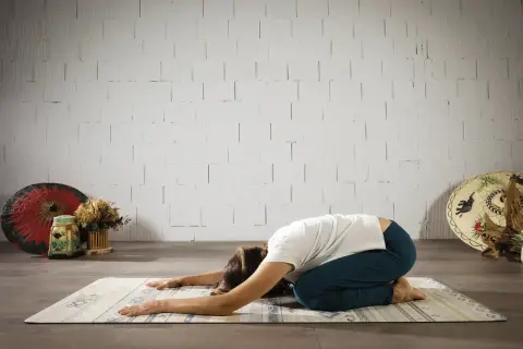 Mujer en postura de niño, buscando el yoga significado espiritual. Relajación y conexión interior.