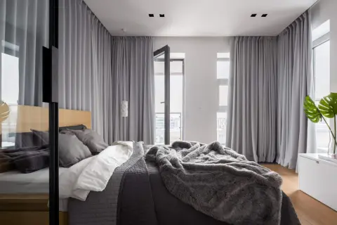 Elegancka sypialnia z dużym łóżkiem, przytulnym futrzanym kocem i szarą zasłoną w oknie, która tworzy przytulną atmosferę.