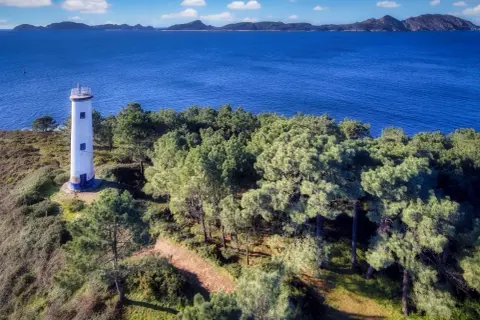 El faro de Cabo Home se alza solitario en una colina verde, vigilando el azul intenso del mar y las islas lejanas.