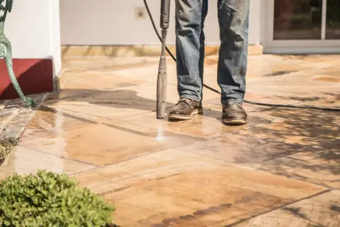 Un homme nettoie un carrelage antidérapant avec un nettoyeur haute pression. L'eau éclabousse sur les dalles.