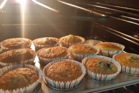 En plåt med nybakade glutenfria muffins i ugnen. Ljuset från ugnen lyser upp de gyllene muffinsarna.